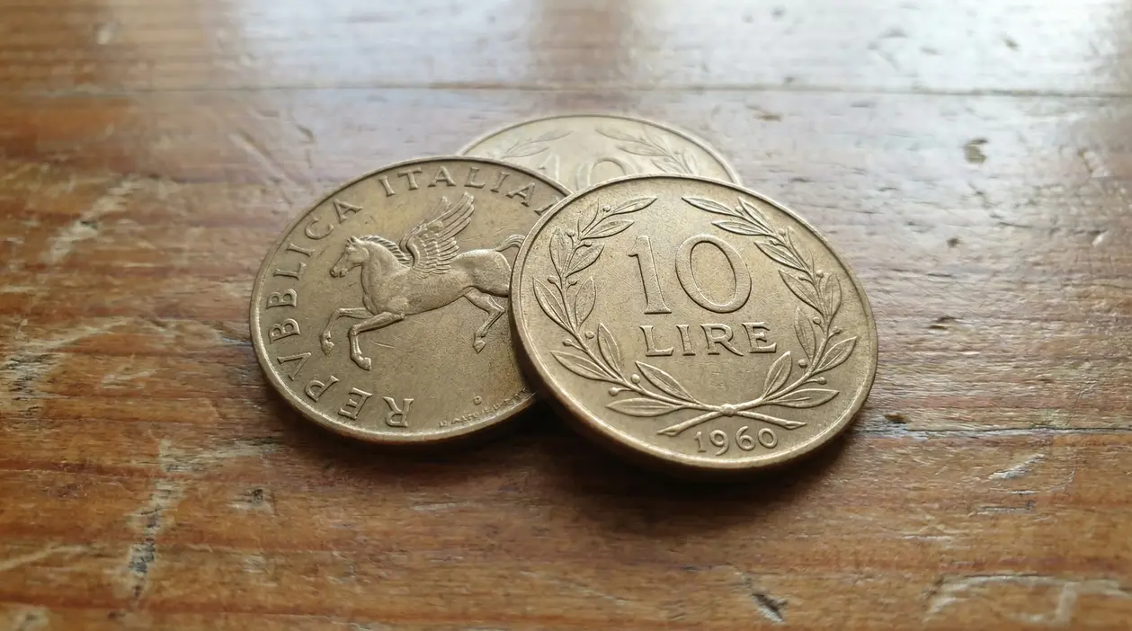 Monete da 10 lire del 1960 appoggiate su una superficie in legno