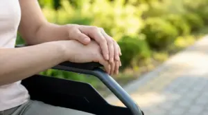 Mani di una persona seduta su una sedia a rotelle in un parco