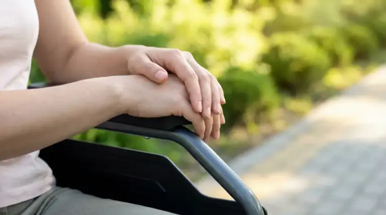 Mani di una persona seduta su una sedia a rotelle in un parco
