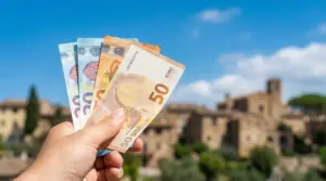 Una mano tiene banconote in euro con un paesaggio italiano sullo sfondo
