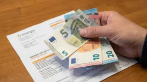 Una mano tiene alcune banconote in euro sopra una bolletta della luce