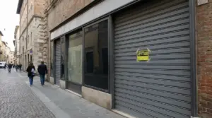 Saracinesca chiusa di un negozio con cartello 'Affittasi' in una strada del centro città