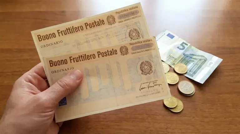 Mano che tiene buoni fruttiferi postali con monete e banconota da cinque euro su tavolo in legno