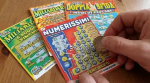 Una persona gratta un biglietto del Gratta e Vinci con una moneta su un tavolo.