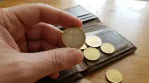 Una mano tiene una moneta da 1 euro con il disegno dell'Uomo Vitruviano davanti a un portafoglio aperto