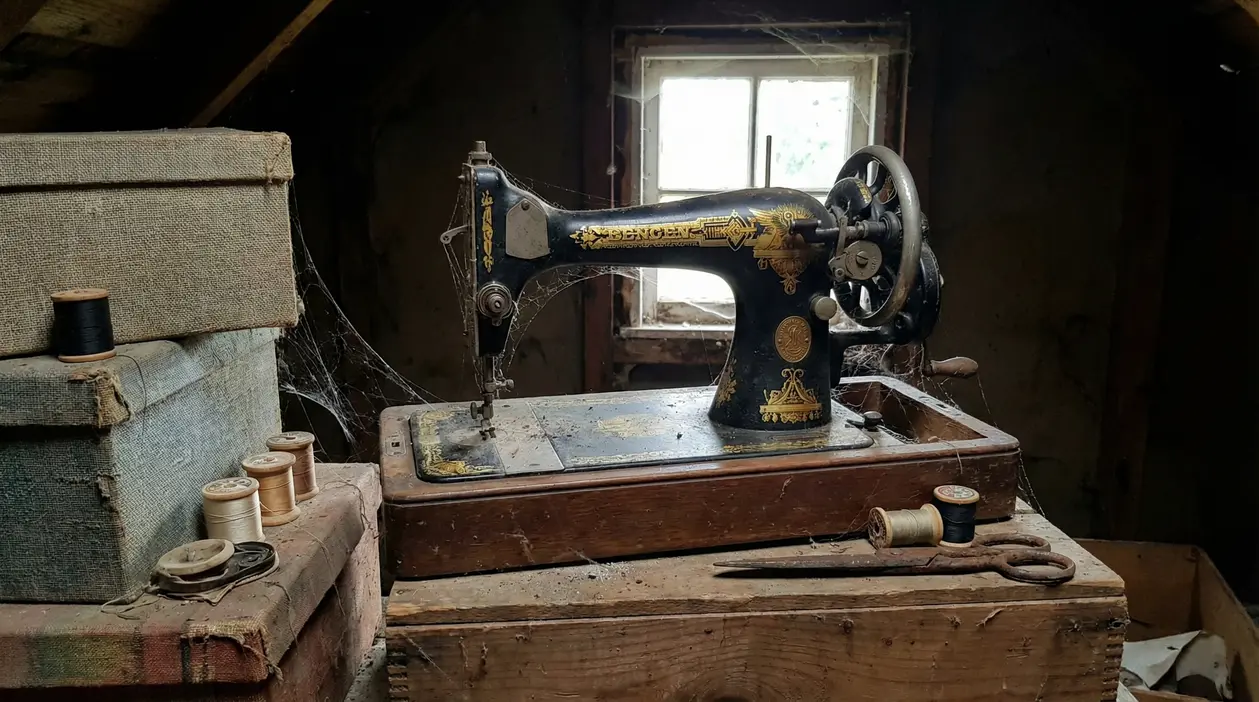 Vecchia macchina da cucire in legno e metallo su un tavolo polveroso in soffitta